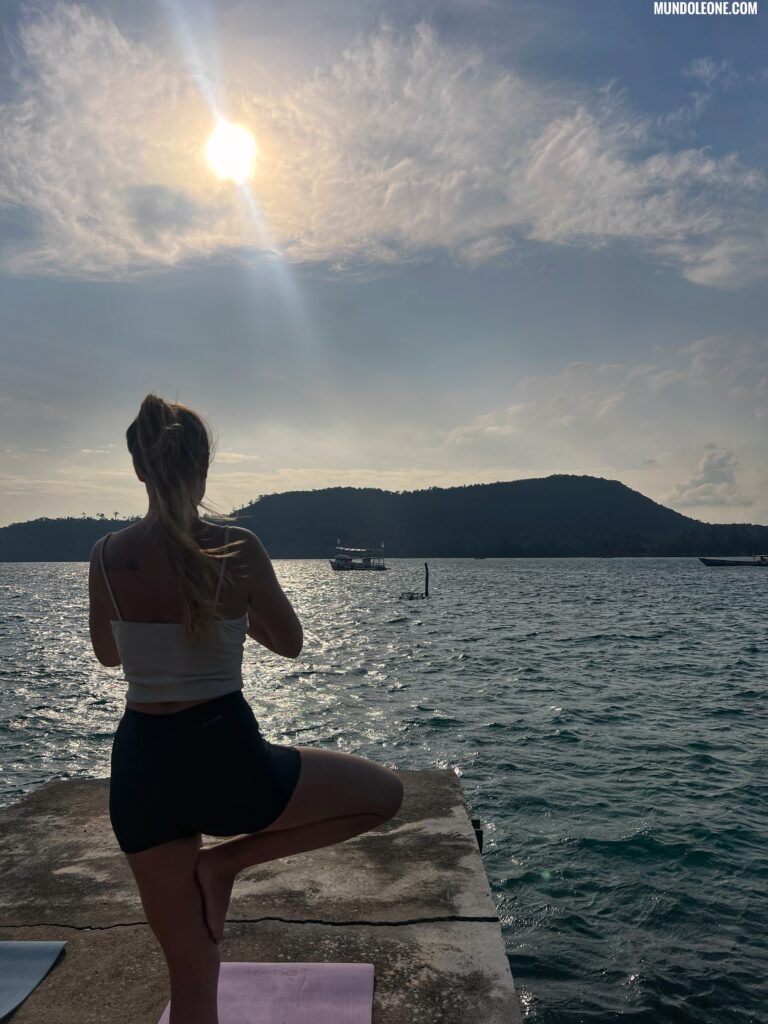 Woman practicing yoga on a wooden pier in M’Pai Bay, Koh Rong Samloem, with local fishing boats.